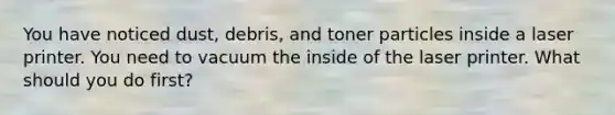 You have noticed dust, debris, and toner particles inside a laser printer. You need to vacuum the inside of the laser printer. What should you do first?
