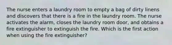 The nurse enters a laundry room to empty a bag of dirty linens and discovers that there is a fire in the laundry room. The nurse activates the alarm, closes the laundry room door, and obtains a fire extinguisher to extinguish the fire. Which is the first action when using the fire extinguisher?