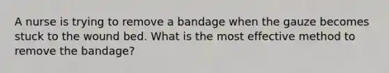 A nurse is trying to remove a bandage when the gauze becomes stuck to the wound bed. What is the most effective method to remove the bandage?