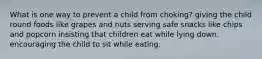 What is one way to prevent a child from choking? giving the child round foods like grapes and nuts serving safe snacks like chips and popcorn insisting that children eat while lying down. encouraging the child to sit while eating.