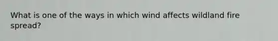 What is one of the ways in which wind affects wildland fire spread?