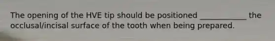 The opening of the HVE tip should be positioned ____________ the occlusal/incisal surface of the tooth when being prepared.