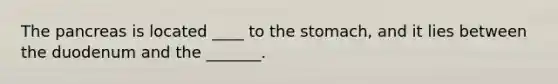 The pancreas is located ____ to the stomach, and it lies between the duodenum and the _______.