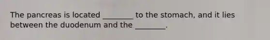 The pancreas is located ________ to the stomach, and it lies between the duodenum and the ________.