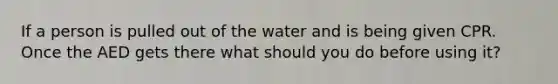 If a person is pulled out of the water and is being given CPR. Once the AED gets there what should you do before using it?