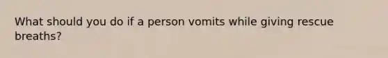 What should you do if a person vomits while giving rescue breaths?