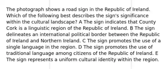 The photograph shows a road sign in the Republic of Ireland. Which of the following best describes the sign's significance within the cultural landscape? A The sign indicates that County Cork is a linguistic region of the Republic of Ireland. B The sign delineates an international political border between the Republic of Ireland and Northern Ireland. C The sign promotes the use of a single language in the region. D The sign promotes the use of traditional language among citizens of the Republic of Ireland. E The sign represents a uniform cultural identity within the region.