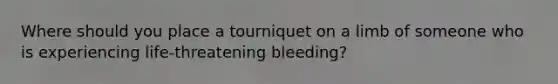 Where should you place a tourniquet on a limb of someone who is experiencing life-threatening bleeding?