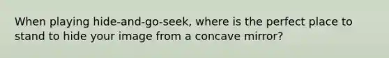 When playing hide-and-go-seek, where is the perfect place to stand to hide your image from a concave mirror?