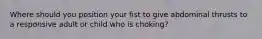 Where should you position your fist to give abdominal thrusts to a responsive adult or child who is choking?