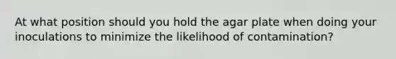 At what position should you hold the agar plate when doing your inoculations to minimize the likelihood of contamination?