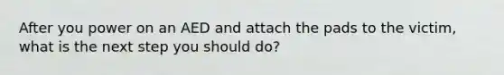 After you power on an AED and attach the pads to the victim, what is the next step you should do?