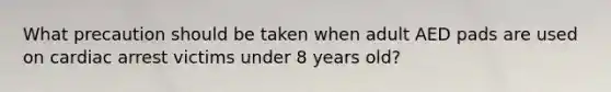 What precaution should be taken when adult AED pads are used on cardiac arrest victims under 8 years old?