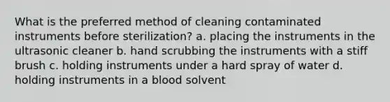 What is the preferred method of cleaning contaminated instruments before sterilization? a. placing the instruments in the ultrasonic cleaner b. hand scrubbing the instruments with a stiff brush c. holding instruments under a hard spray of water d. holding instruments in a blood solvent