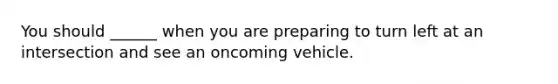 You should ______ when you are preparing to turn left at an intersection and see an oncoming vehicle.