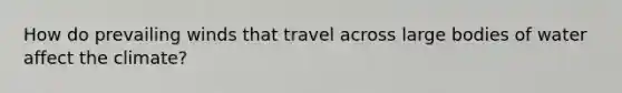 How do prevailing winds that travel across large bodies of water affect the climate?