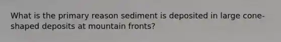 What is the primary reason sediment is deposited in large cone-shaped deposits at mountain fronts?