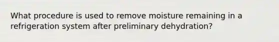 What procedure is used to remove moisture remaining in a refrigeration system after preliminary dehydration?