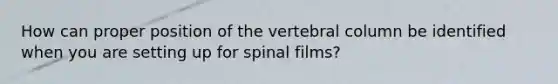 How can proper position of the vertebral column be identified when you are setting up for spinal films?