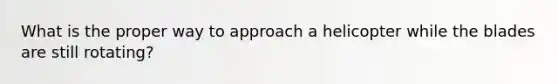 What is the proper way to approach a helicopter while the blades are still rotating?