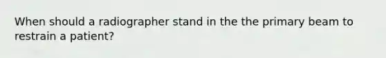 When should a radiographer stand in the the primary beam to restrain a patient?