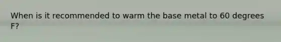 When is it recommended to warm the base metal to 60 degrees F?