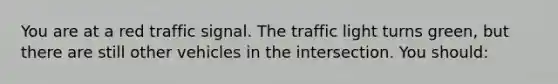 You are at a red traffic signal. The traffic light turns green, but there are still other vehicles in the intersection. You should: