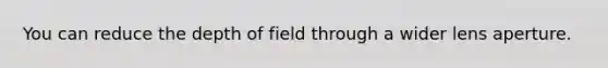 You can reduce the depth of field through a wider lens aperture.