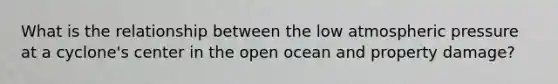 What is the relationship between the low atmospheric pressure at a cyclone's center in the open ocean and property damage?