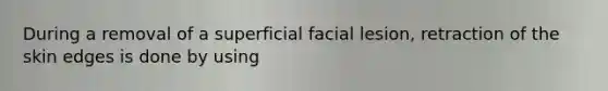 During a removal of a superficial facial lesion, retraction of the skin edges is done by using