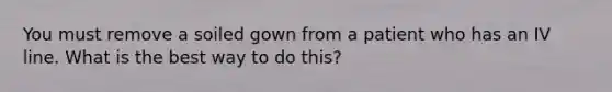 You must remove a soiled gown from a patient who has an IV line. What is the best way to do this?