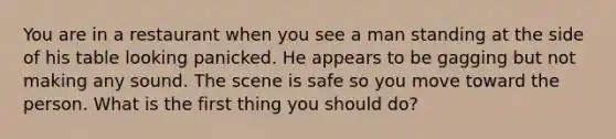 You are in a restaurant when you see a man standing at the side of his table looking panicked. He appears to be gagging but not making any sound. The scene is safe so you move toward the person. What is the first thing you should do?