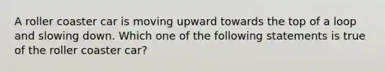 A roller coaster car is moving upward towards the top of a loop and slowing down. Which one of the following statements is true of the roller coaster car?