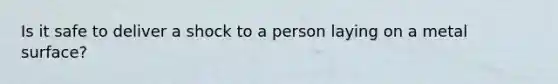 Is it safe to deliver a shock to a person laying on a metal surface?