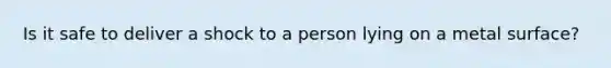 Is it safe to deliver a shock to a person lying on a metal surface?