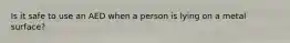 Is it safe to use an AED when a person is lying on a metal surface?