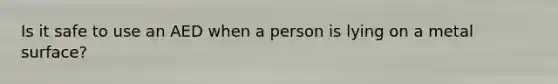 Is it safe to use an AED when a person is lying on a metal surface?