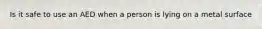 Is it safe to use an AED when a person is lying on a metal surface