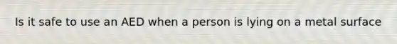 Is it safe to use an AED when a person is lying on a metal surface