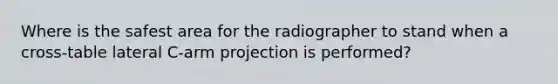 Where is the safest area for the radiographer to stand when a cross-table lateral C-arm projection is performed?