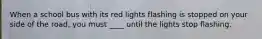 When a school bus with its red lights flashing is stopped on your side of the road, you must ____ until the lights stop flashing.