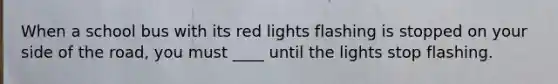 When a school bus with its red lights flashing is stopped on your side of the road, you must ____ until the lights stop flashing.