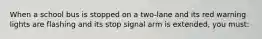 When a school bus is stopped on a two-lane and its red warning lights are flashing and its stop signal arm is extended, you must: