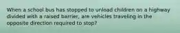 When a school bus has stopped to unload children on a highway divided with a raised barrier, are vehicles traveling in the opposite direction required to stop?