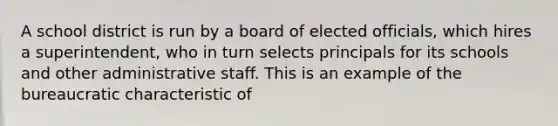 A school district is run by a board of elected officials, which hires a superintendent, who in turn selects principals for its schools and other administrative staff. This is an example of the bureaucratic characteristic of