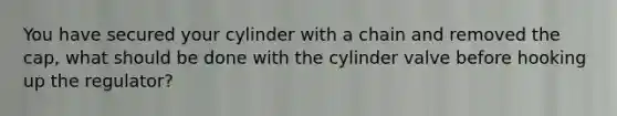 You have secured your cylinder with a chain and removed the cap, what should be done with the cylinder valve before hooking up the regulator?