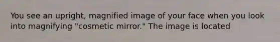 You see an upright, magnified image of your face when you look into magnifying "cosmetic mirror." The image is located