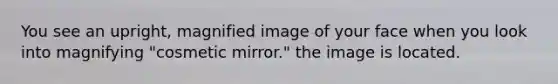 You see an upright, magnified image of your face when you look into magnifying "cosmetic mirror." the image is located.