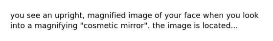 you see an upright, magnified image of your face when you look into a magnifying "cosmetic mirror". the image is located...