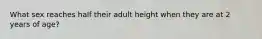 What sex reaches half their adult height when they are at 2 years of age?